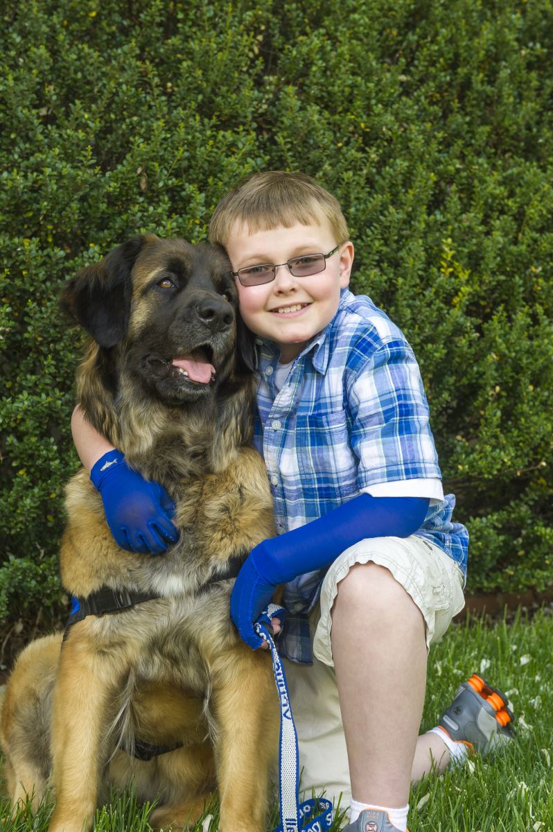 Little boy with compression gloves hugs his dog