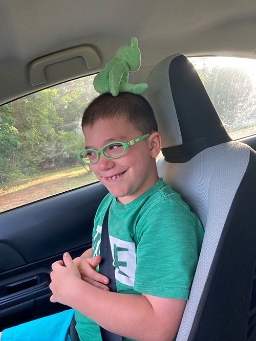 CHoR patient Graden smiling in the car with a green stuffed animal on his head