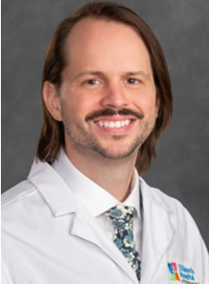 Headshot of Griffin Shoemaker wearing a white physicians coat over a white collared shot and a multi-colored, teal and gray tie.
