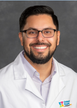 Headshot of Cristian Jarmillo wearing a white physicians coat over a light grey collared shirt.