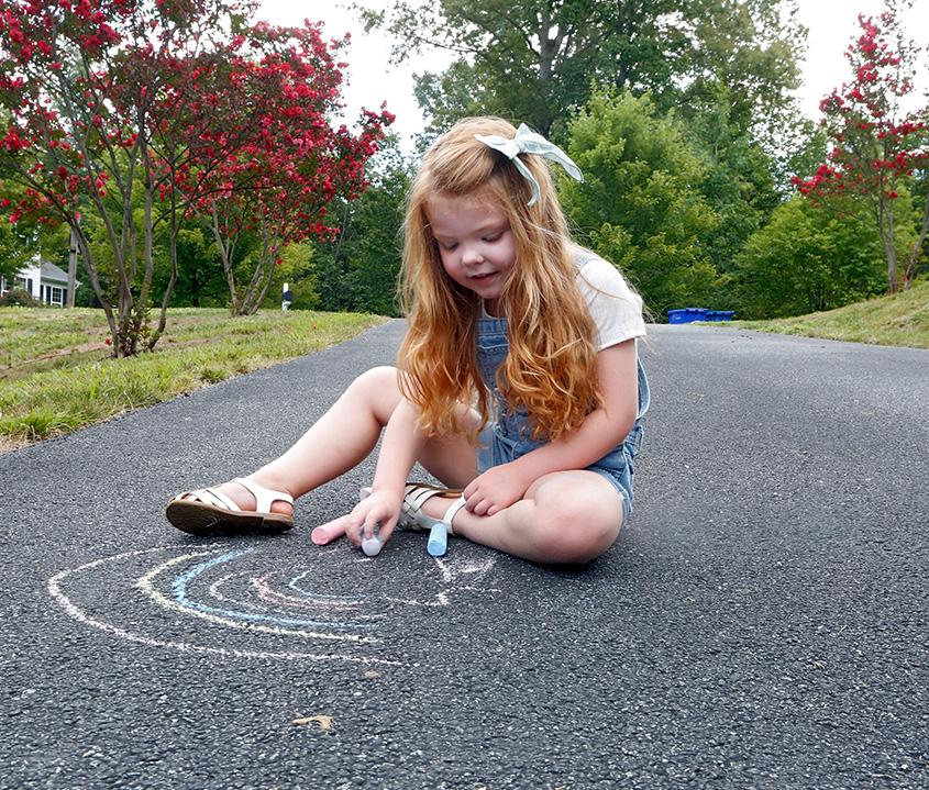 Girl draws with chalk on asphalt